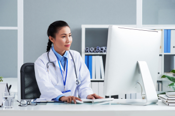 asian doctor with stethoscope around neck sitting office working computer 1